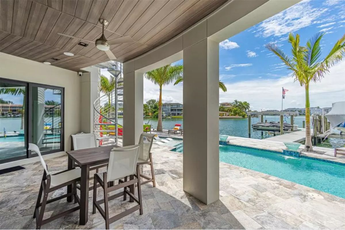 Covered outdoor patio with stone tile flooring overlooks the pool and waterway.