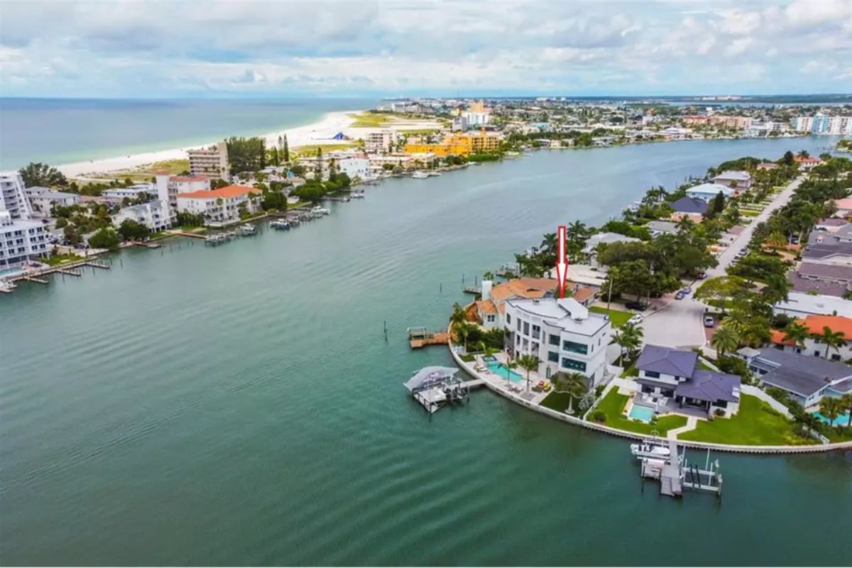 Aerial view of a waterfront neighborhood showing a modern home with a wraparound seawall and private dock.