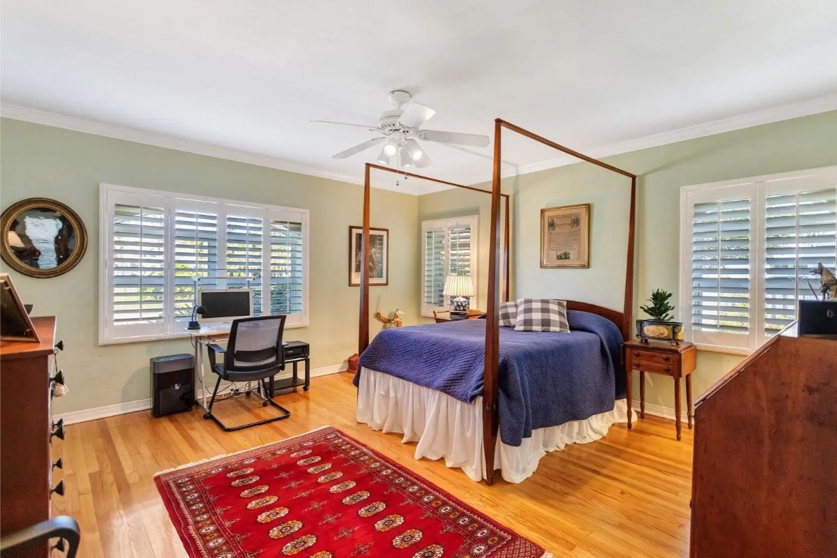 Wooden four-poster bed sits on a red patterned rug with blue bedding.