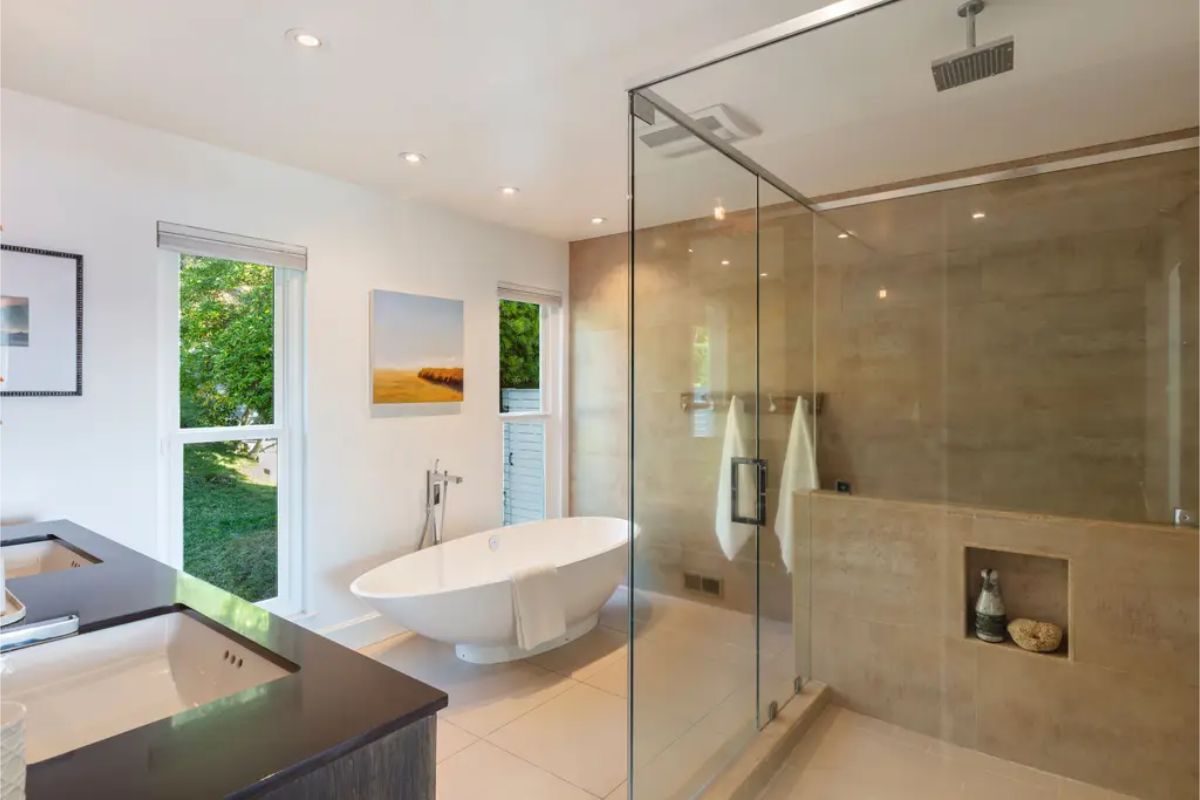 Luxurious bathroom with a glass-enclosed shower, freestanding bathtub, and large windows bringing in natural light. 
