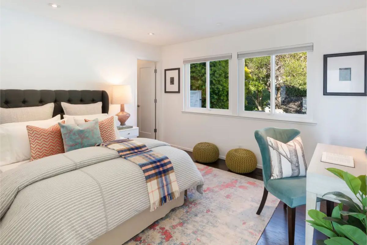 Cozy bedroom with a soft color scheme, a reading nook, and large windows bringing in natural light. 