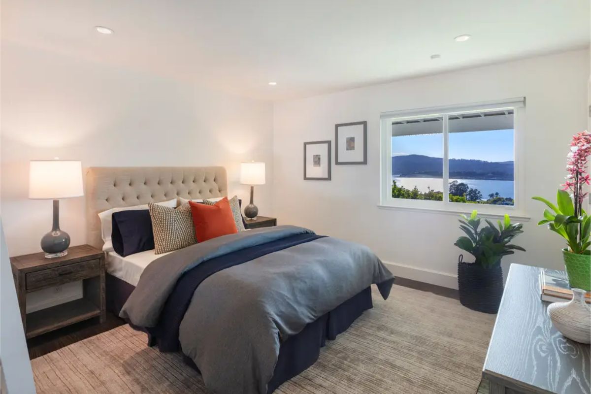 Inviting bedroom with a tufted headboard, warm accents, and a scenic window view of the lake. 