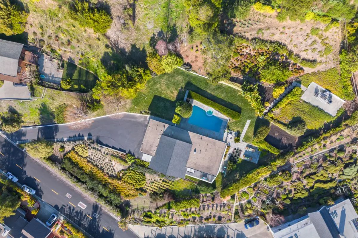 Aerial view of the entire property, showcasing the home, pool, and surrounding greenery in a private hillside setting. 