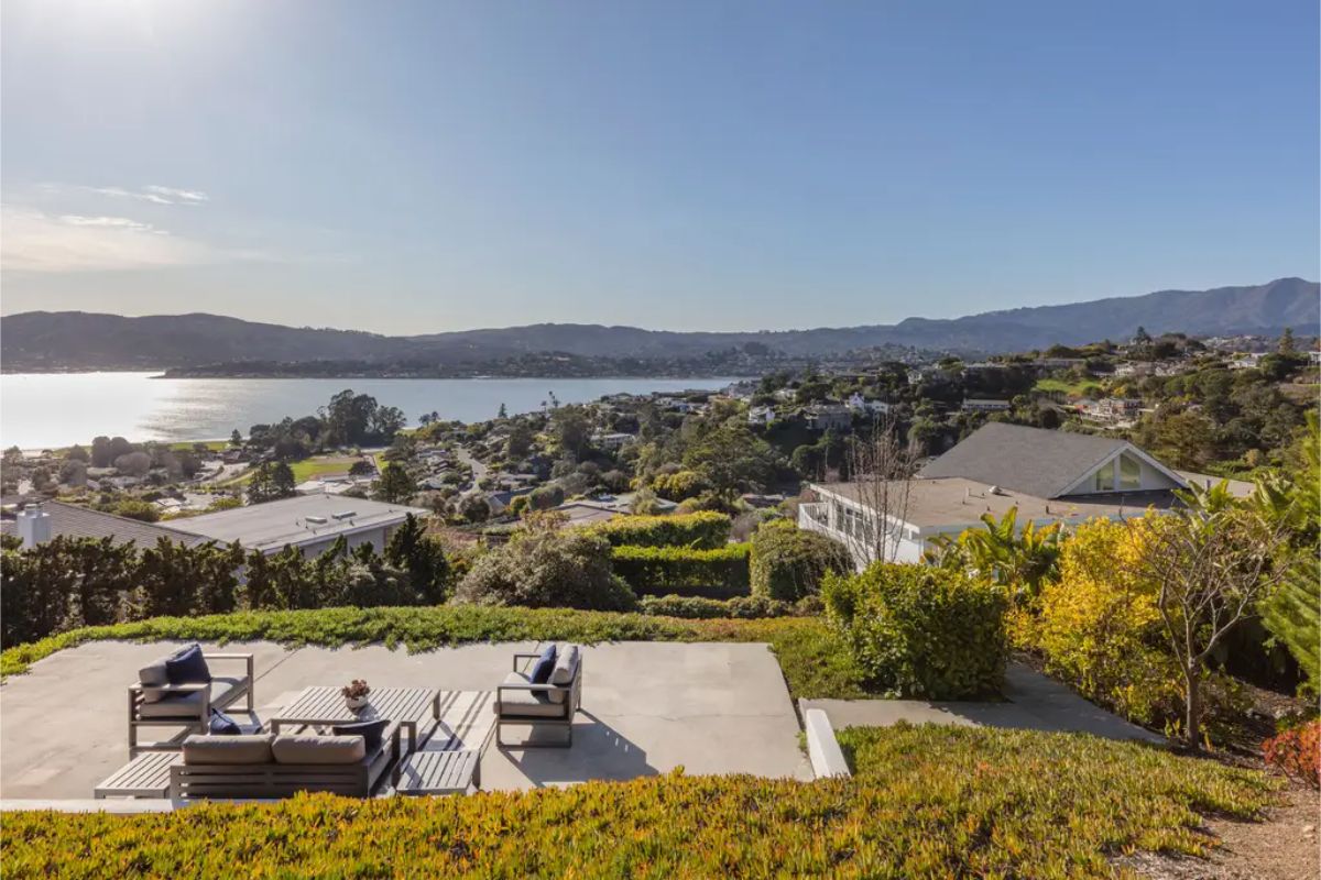 Elevated patio area with multiple seating arrangements, overlooking a picturesque hillside neighborhood and water views. 