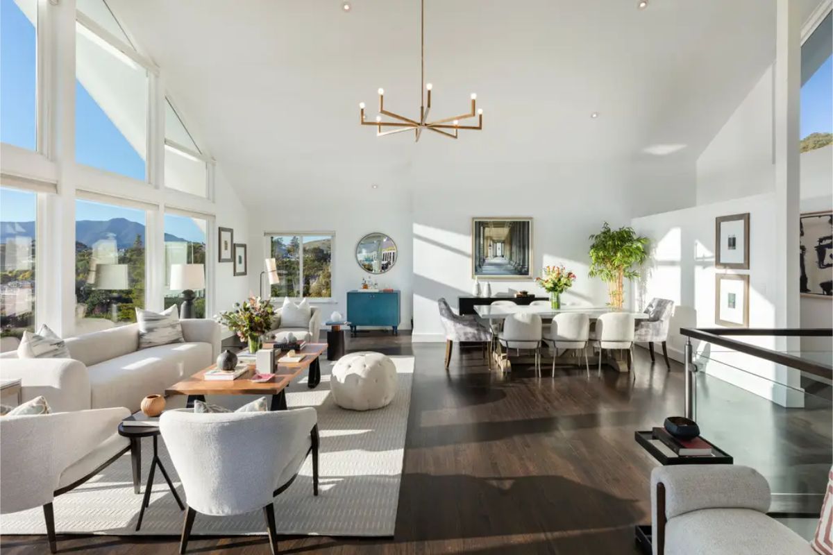 Open-concept living and dining area with elegant furnishings, a minimalist chandelier, and abundant natural light. 
