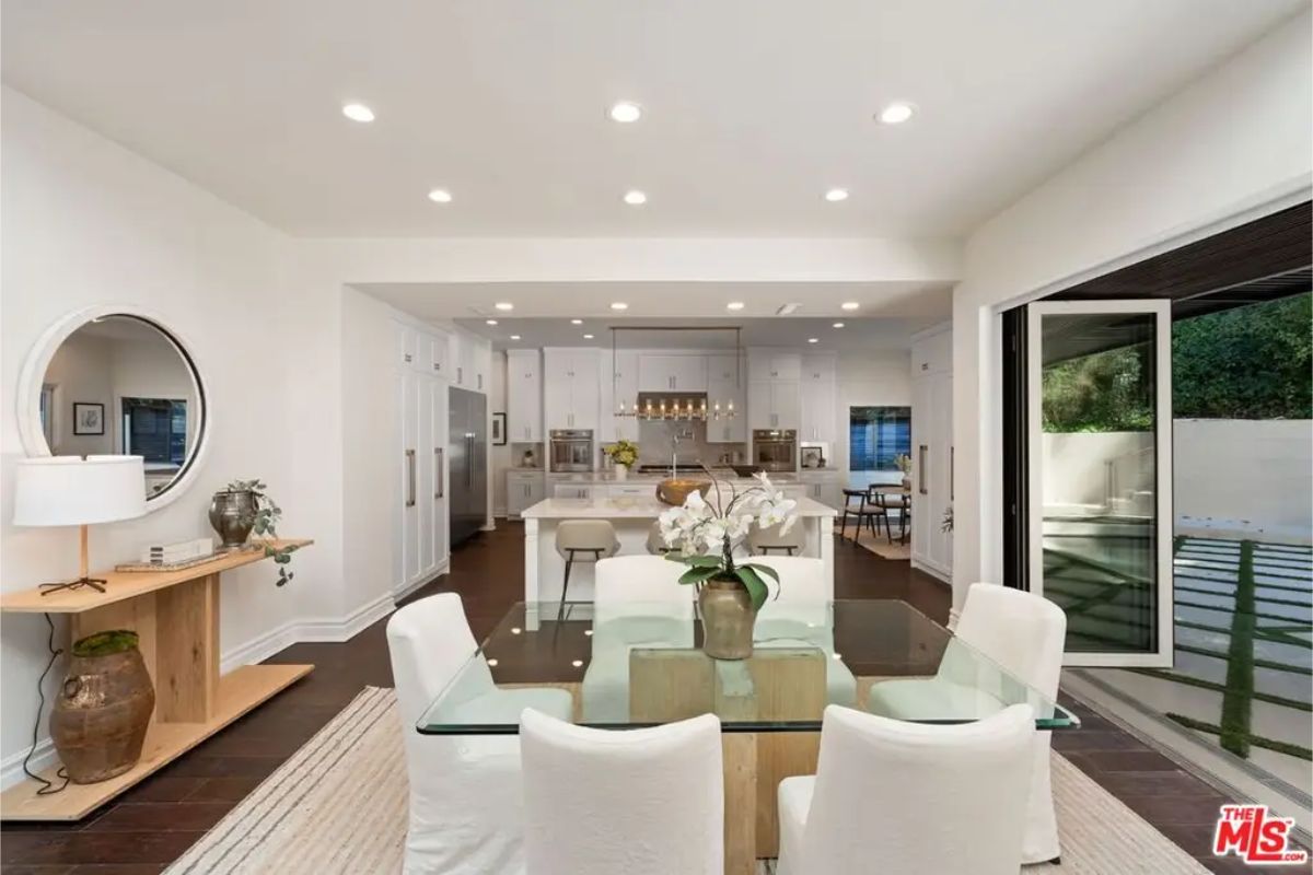 Stylish open-concept kitchen and dining space with sleek white cabinetry and a glass table. 