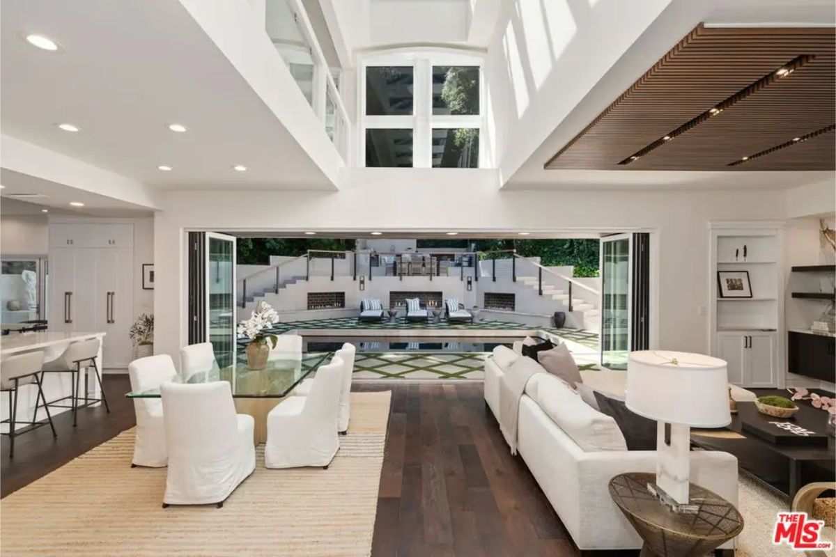 Open-concept living space with high ceilings, white furnishings, and seamless indoor-outdoor flow. 