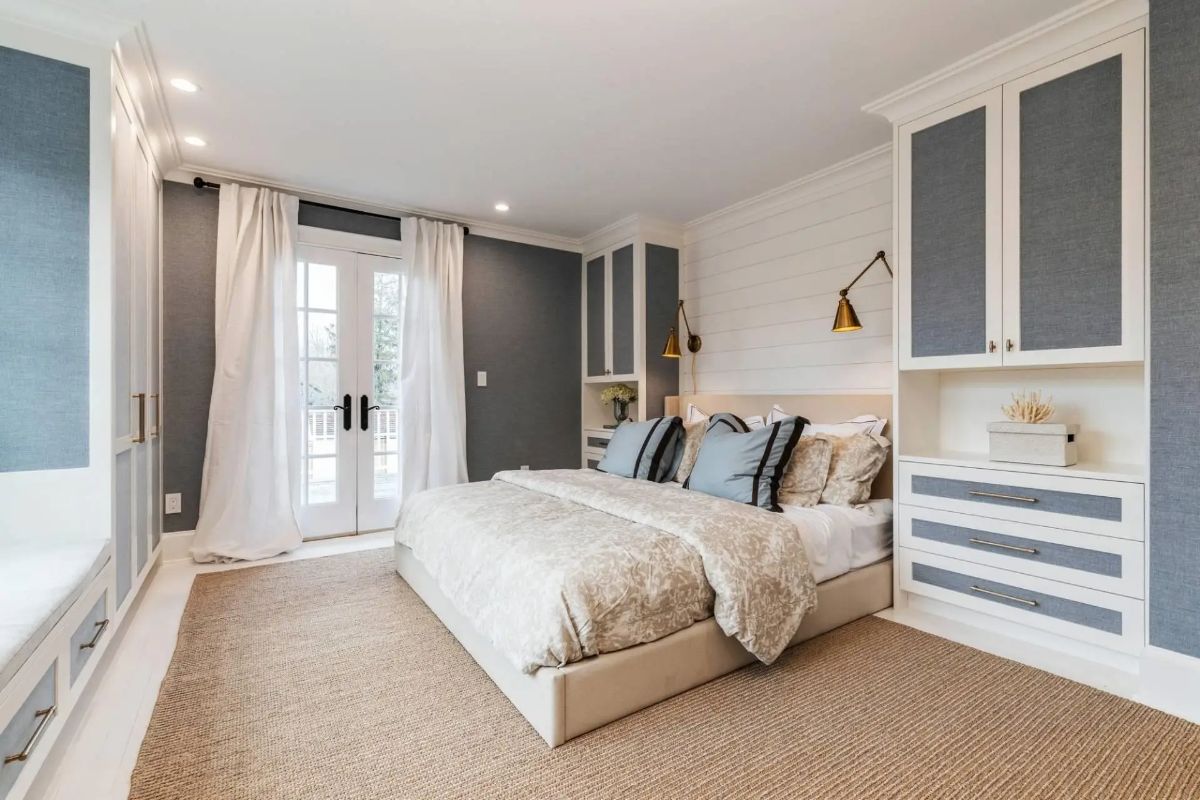 Neutral bed with textured bedding is flanked by built-in closets and reading sconces.