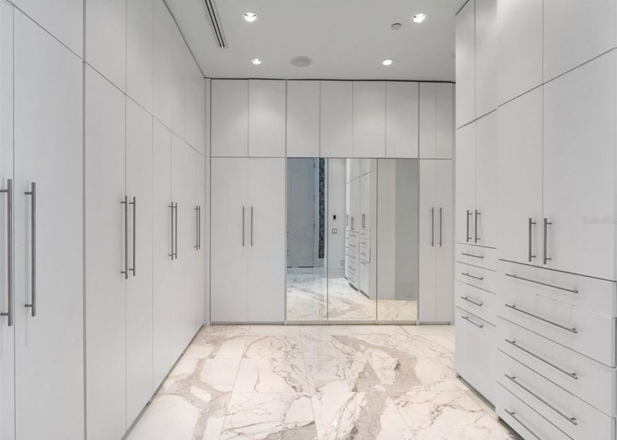 Sleek walk-in closet with white cabinetry, mirrored accents, and marble flooring. 
