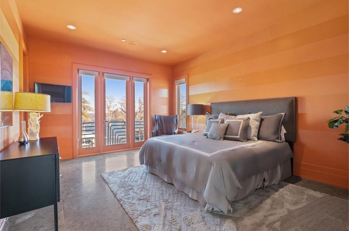 Vibrant bedroom with bold orange walls, a plush gray bed, and access to a balcony with scenic views. 