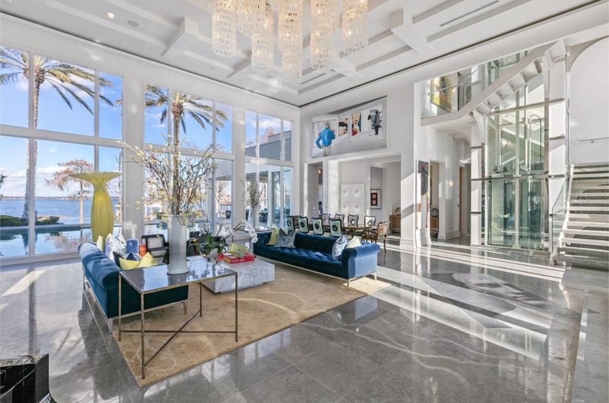 Luxurious living room featuring high ceilings, a glass elevator, large windows, and stylish furniture. 