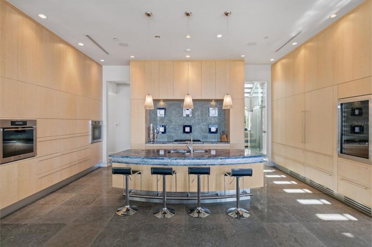 High-end kitchen with a curved island, built-in ovens, and light wood cabinetry. 