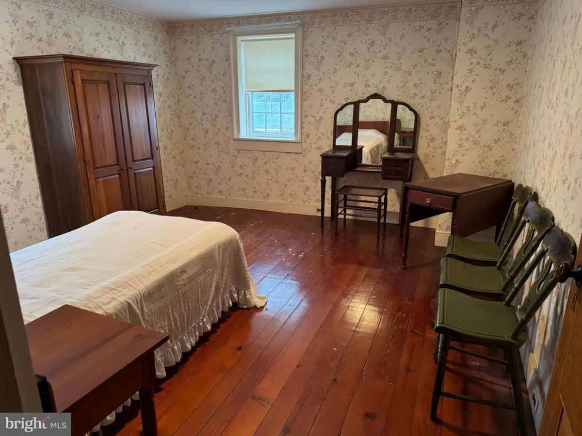 Bedroom with wide-plank hardwood floors and floral wallpaper.