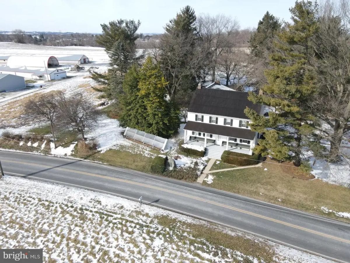 Large white house with a dark roof sits along a two-lane road.