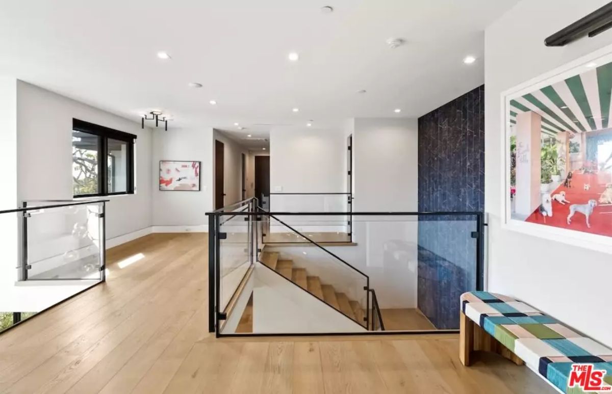 Spacious upper-level hallway with a modern glass railing and wooden flooring. 