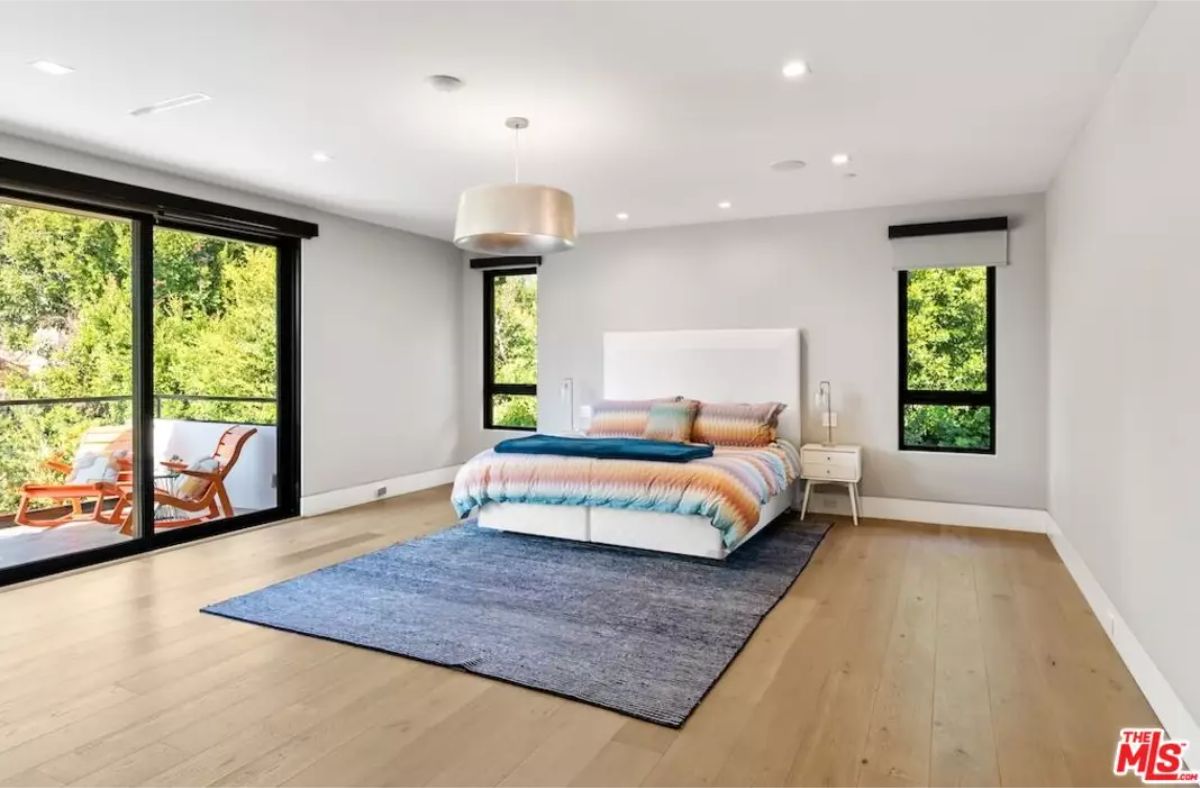 Large bedroom with floor-to-ceiling windows and a private balcony overlooking greenery. 