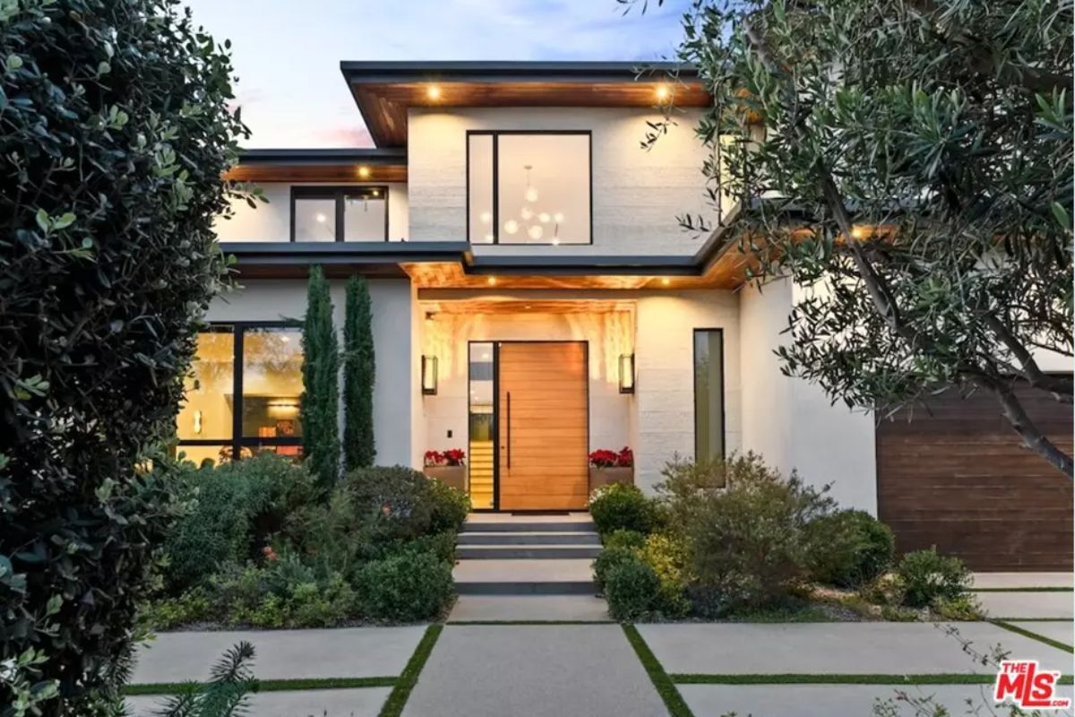 Beautiful entrance is framed by warm exterior lighting and lush landscaping. 