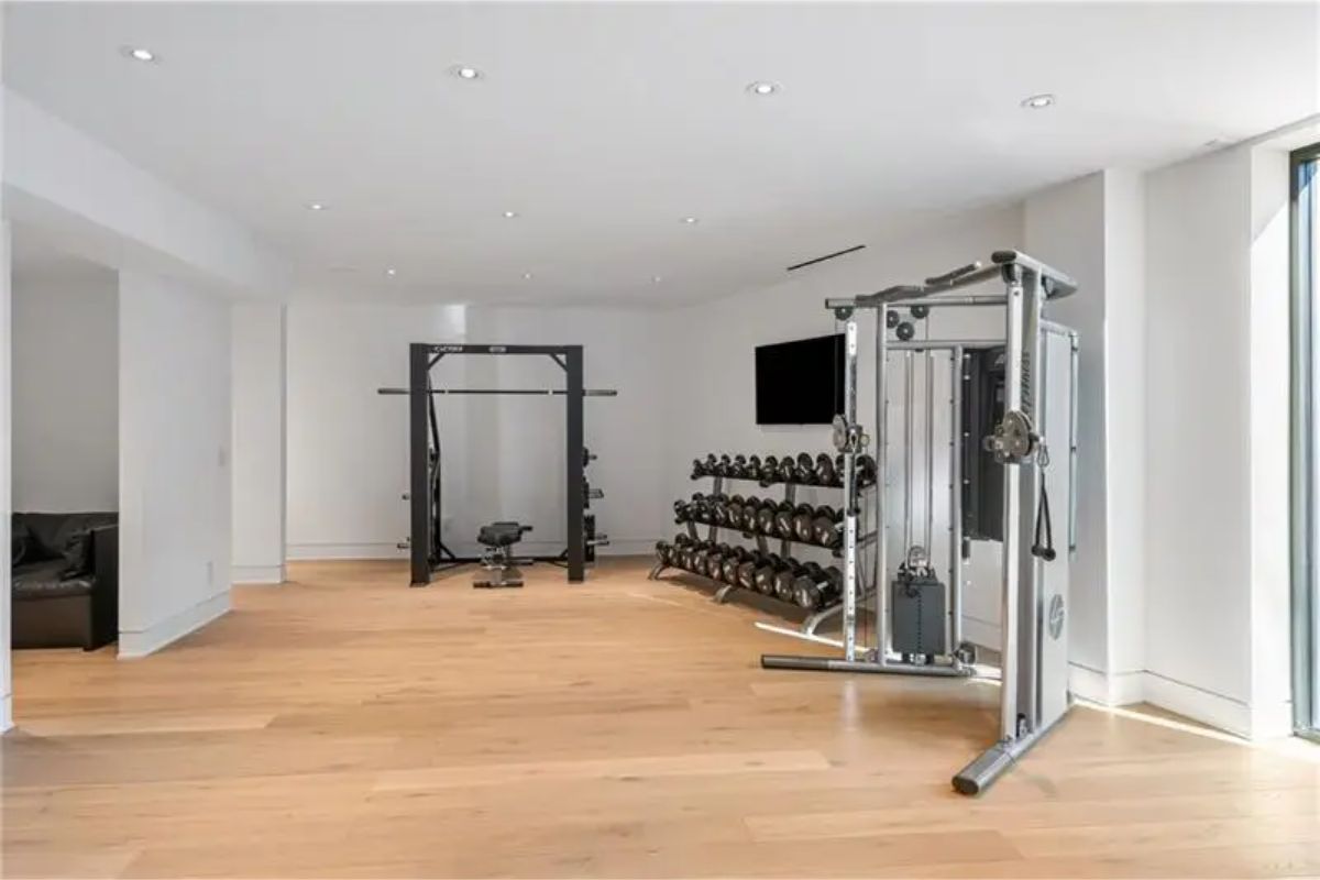 Home gym is equipped with strength training machines, free weights, and large windows for natural light. 