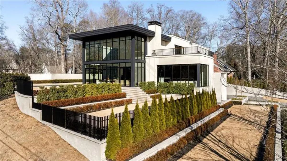 This modern hillside home features striking black-framed glass walls, layered terraced landscaping,