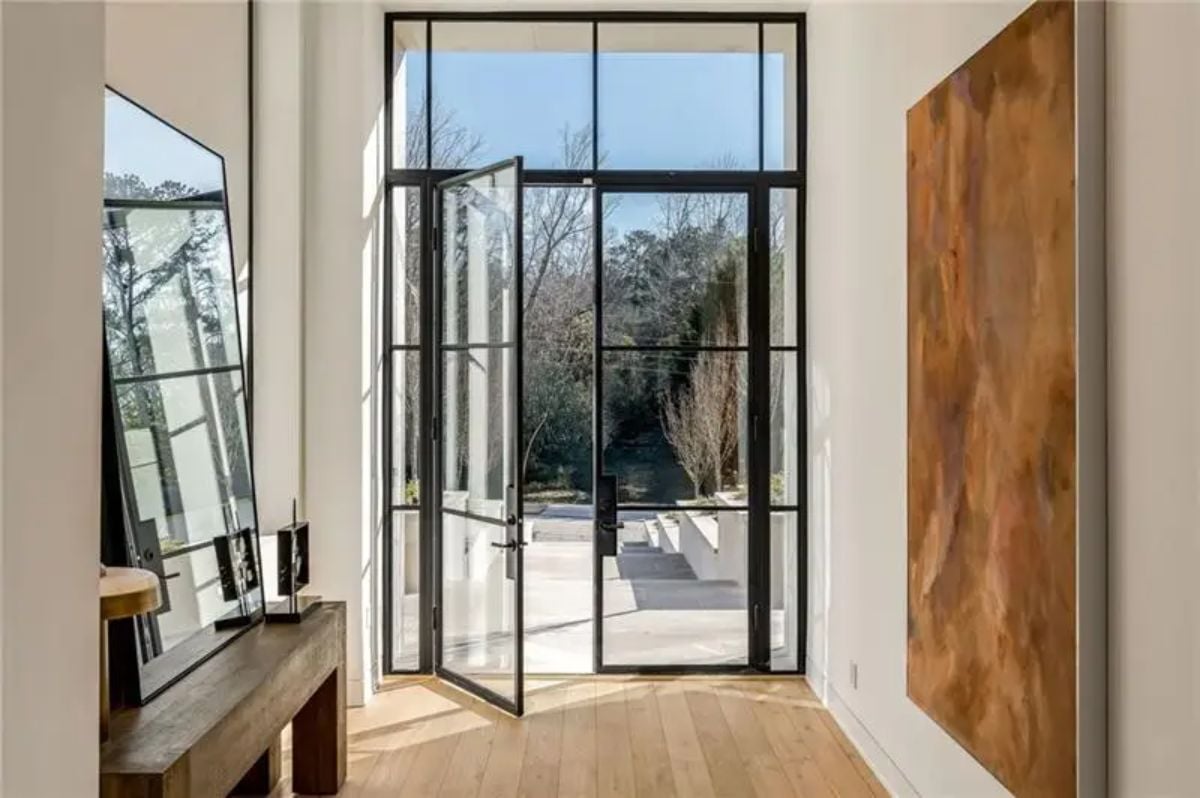 A bright, airy foyer features a pivot glass door with steel framing, welcoming natural light. 