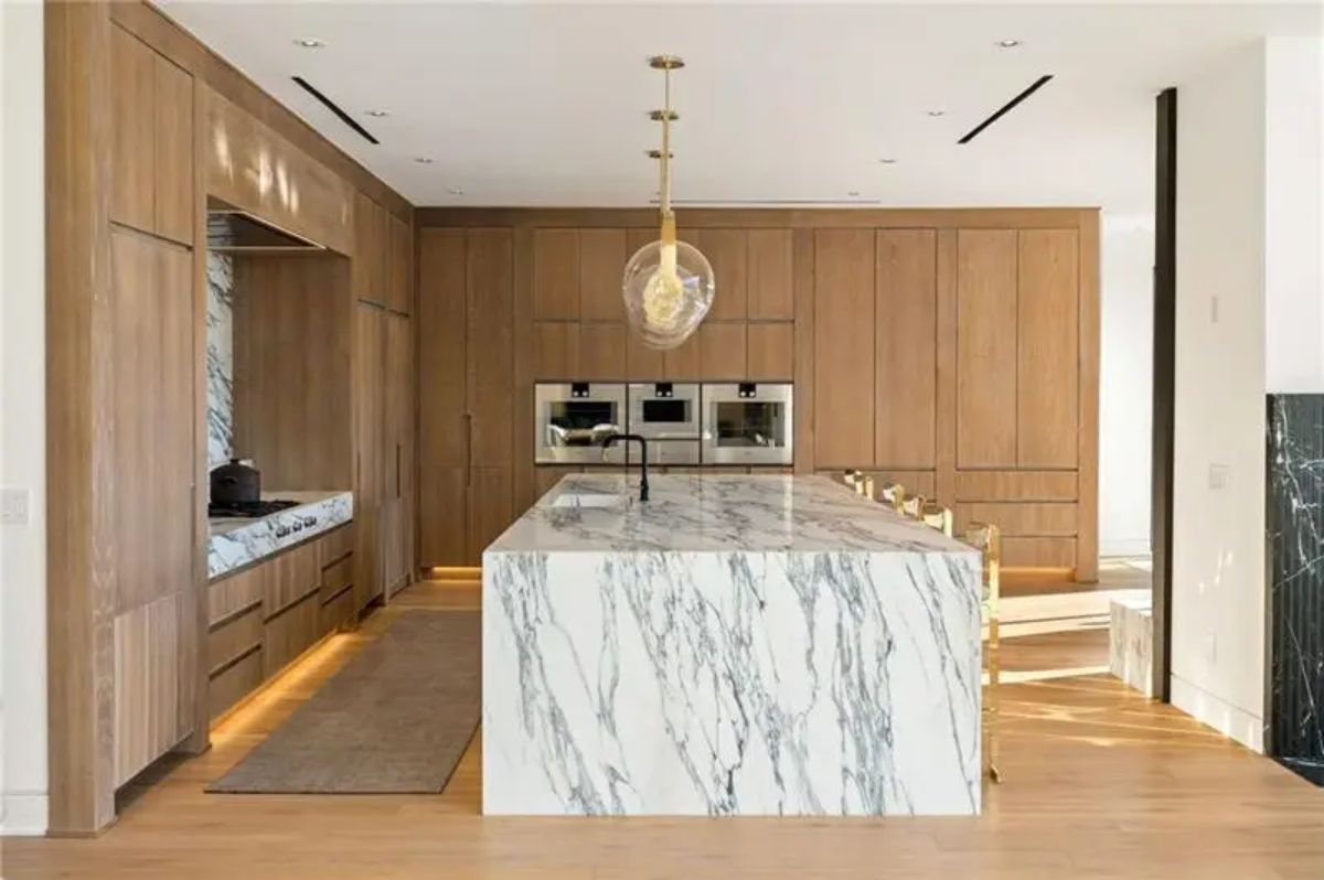 The kitchen stuns with floor-to-ceiling cabinetry, built-in appliances, and a marble waterfall island. 