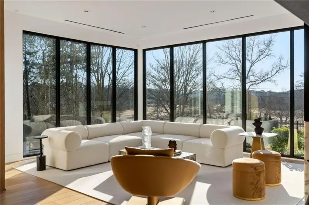 Bright corner lounge space includes floor-to-ceiling windows, a curved white sectional, and sculptural accent furniture. 