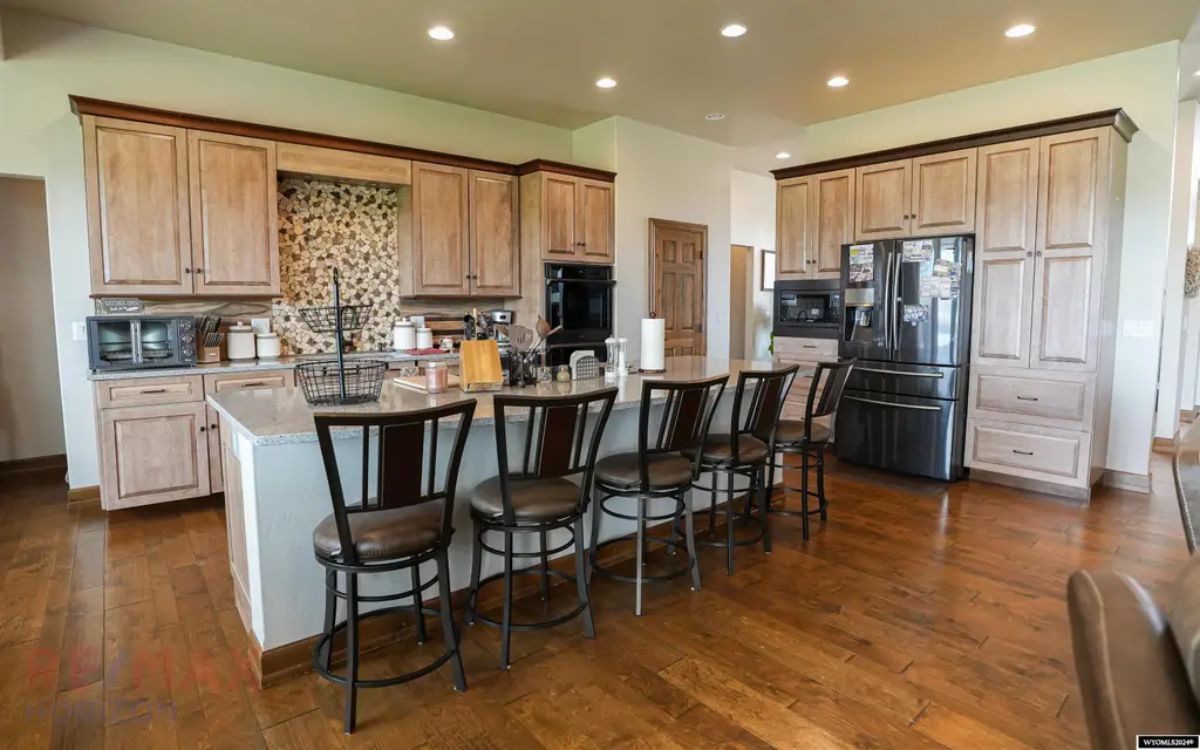 Light wood cabinetry contrasts with dark appliances and a stone tile backsplash.