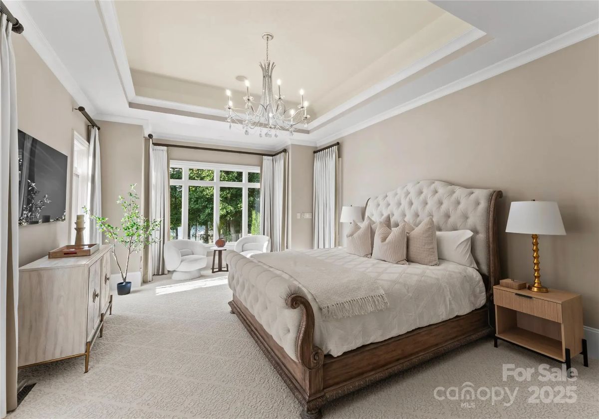 Spacious bedroom with tray ceiling, chandelier, upholstered bed, and large windows bringing in natural light.
