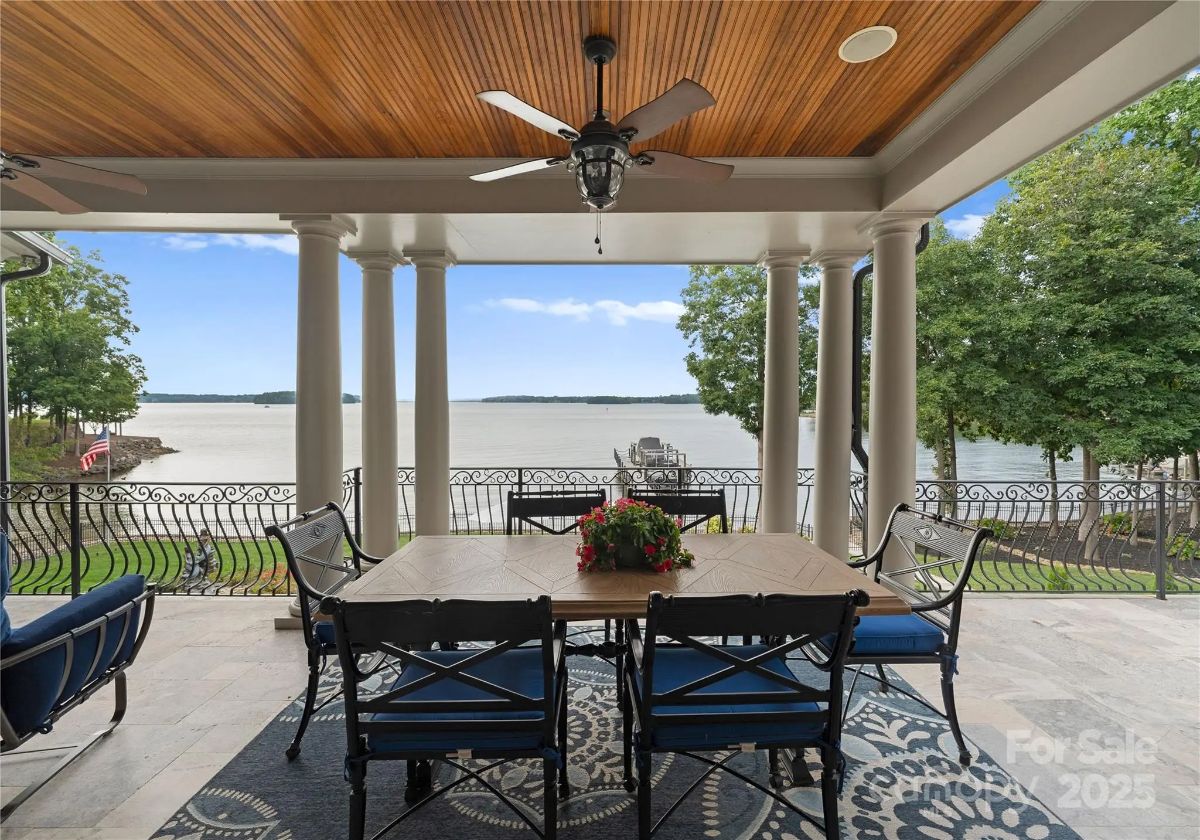 Outdoor dining space under a wood-paneled ceiling with columns and lake views.