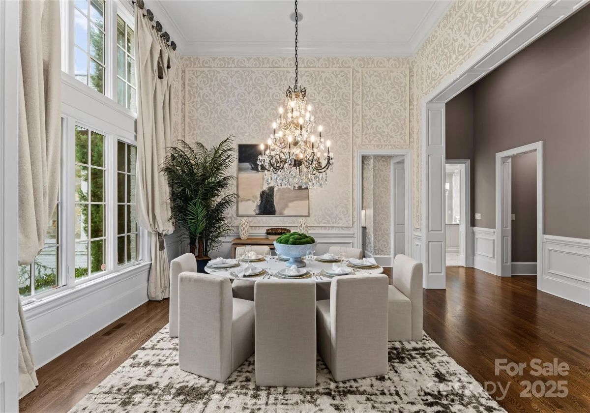 Formal dining room with patterned wallpaper, large chandelier, and tall windows. 