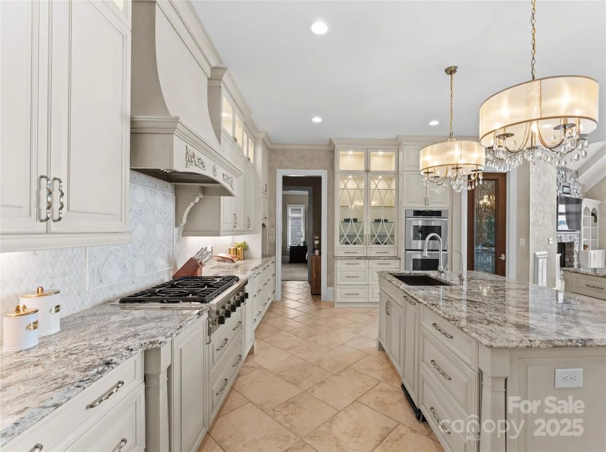 Alternate view of kitchen highlighting stove area, chandeliers, and detailed cabinetry.