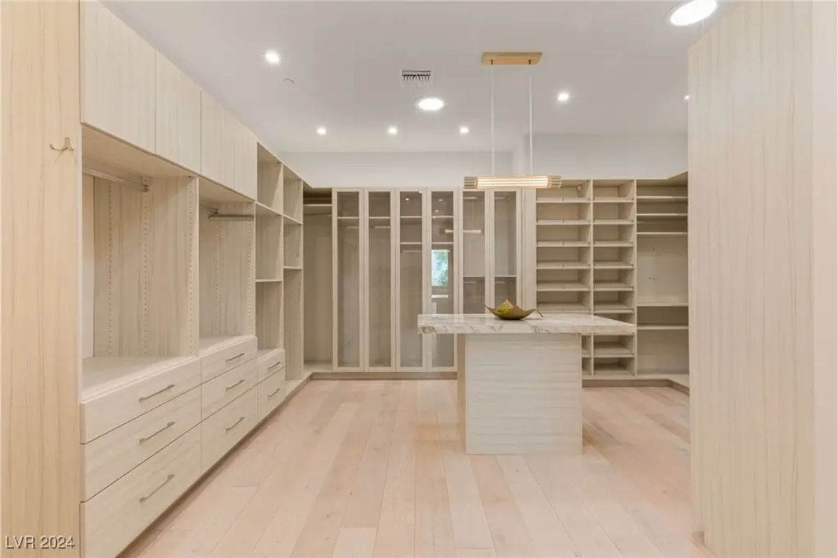 A spacious walk-in closet with built-in shelving, light wood finishes, and a center island for added storage and organization. 