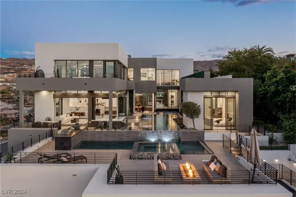 A contemporary luxury home boasts an expansive terrace, a central fire pit, and an elegant outdoor pool area at twilight. 