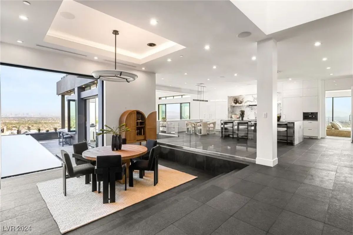 An elegant dining area with a sunken floor design, black flooring, and an open layout leading into the kitchen and living spaces. 