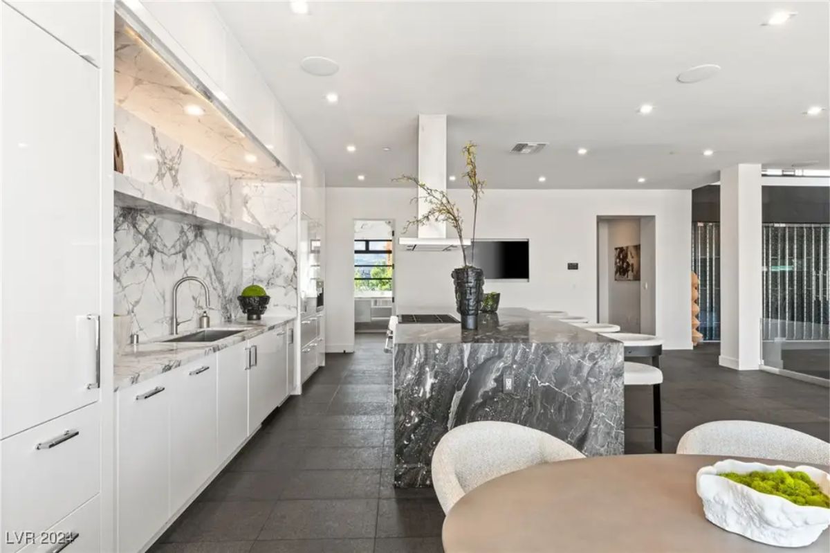 A contemporary kitchen with white cabinetry, a marble backsplash, and a dark granite island, offering a sophisticated cooking and dining experience. 