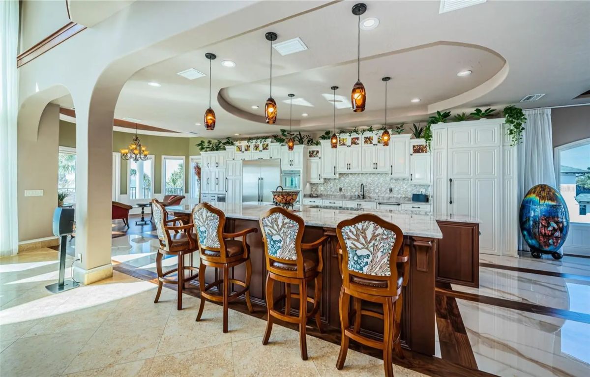 Kitchen has an oversized island with carved wooden barstools and granite countertops.