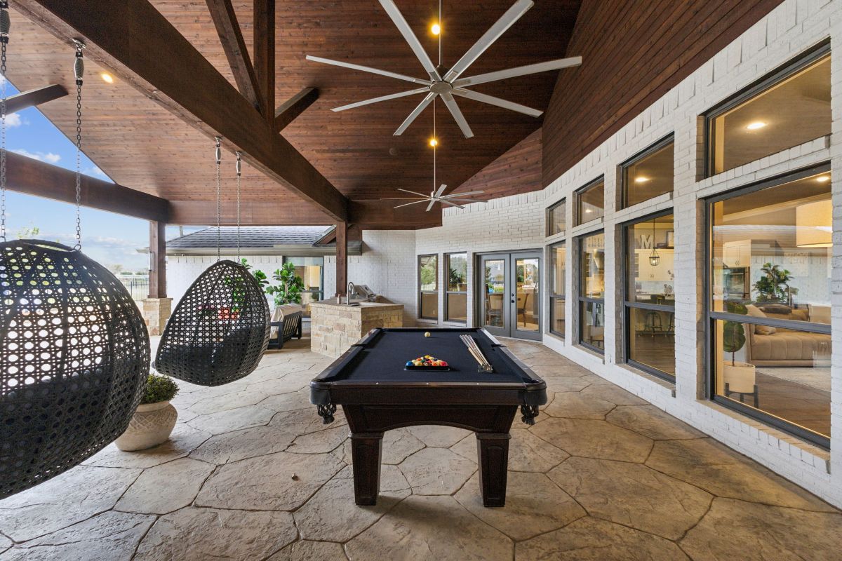 Stone-covered patio has a pool table centered beneath oversized ceiling fans.
