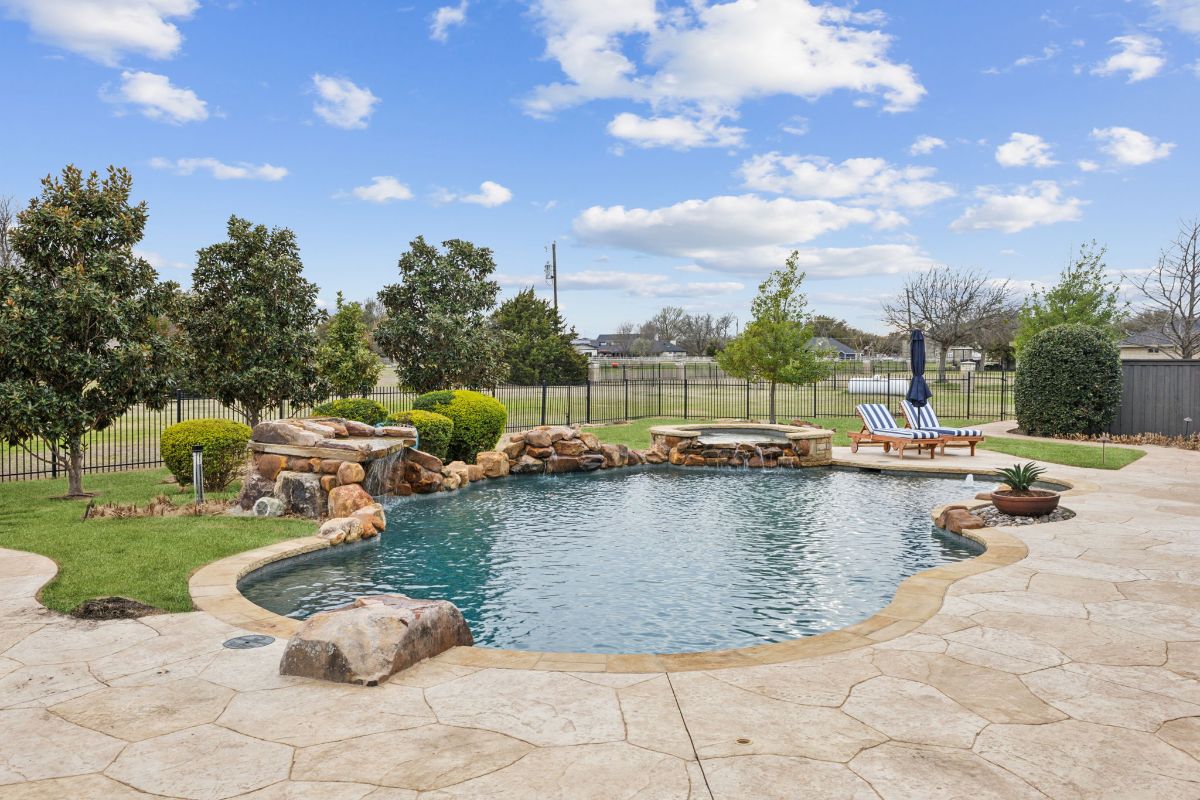 Curved pool is edged with natural stone and surrounded by landscaping.