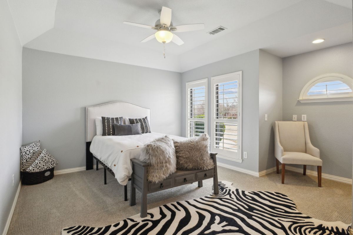 Upholstered bed sits across from shuttered windows.