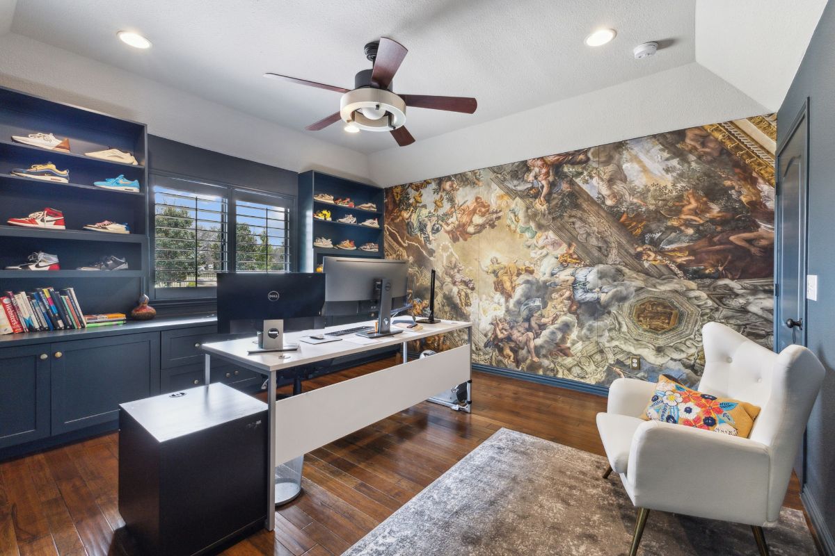 Desk sits centered beneath a ceiling fan with a large monitor setup.