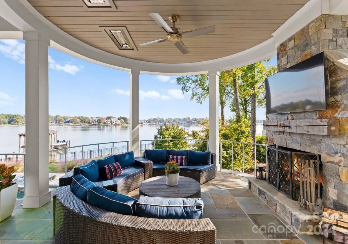 Covered patio includes curved seating, fireplace, ceiling fan, and lakeside views. 