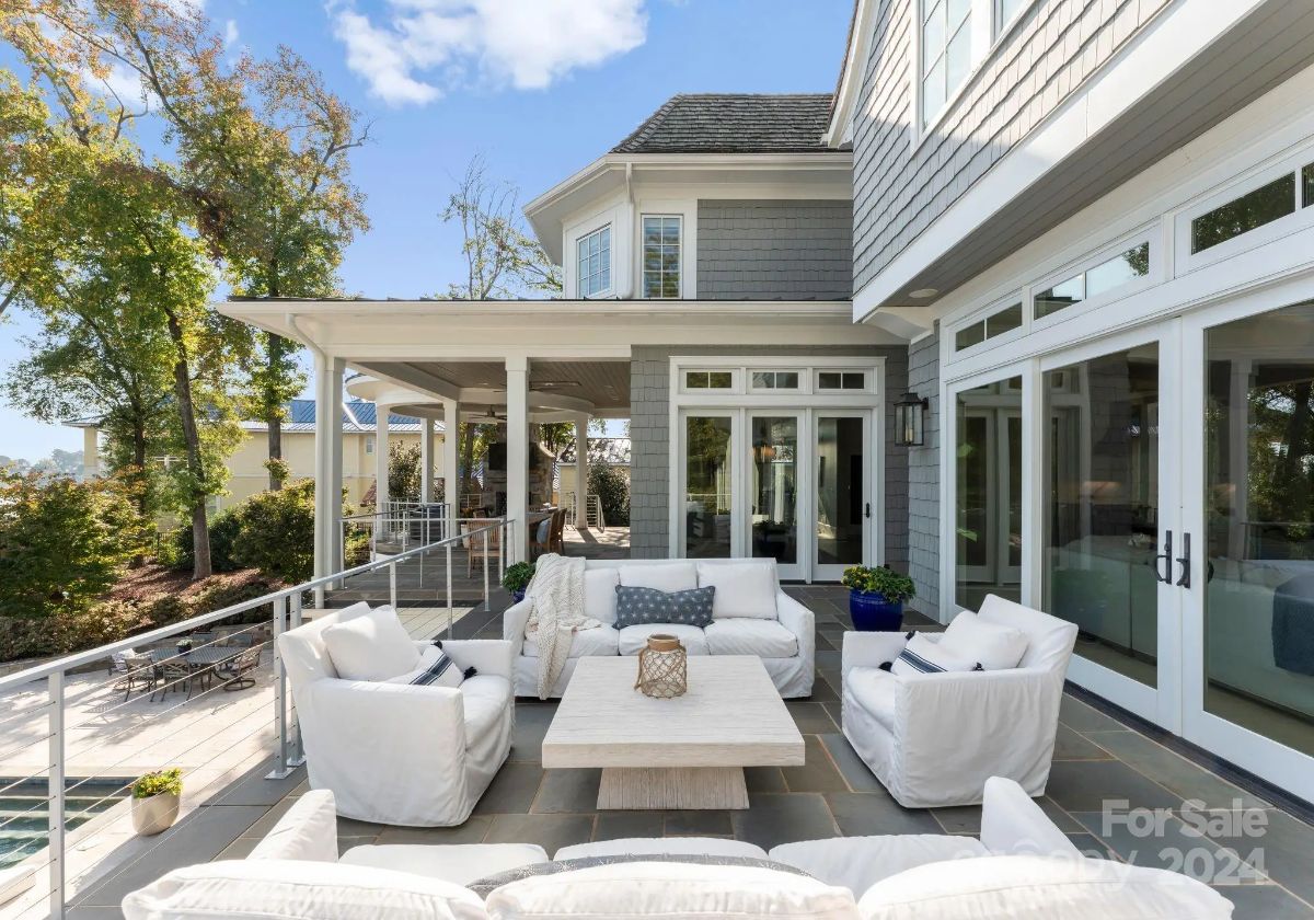 Outdoor lounge area boasts plush white furniture and glass railing with access to the home. 