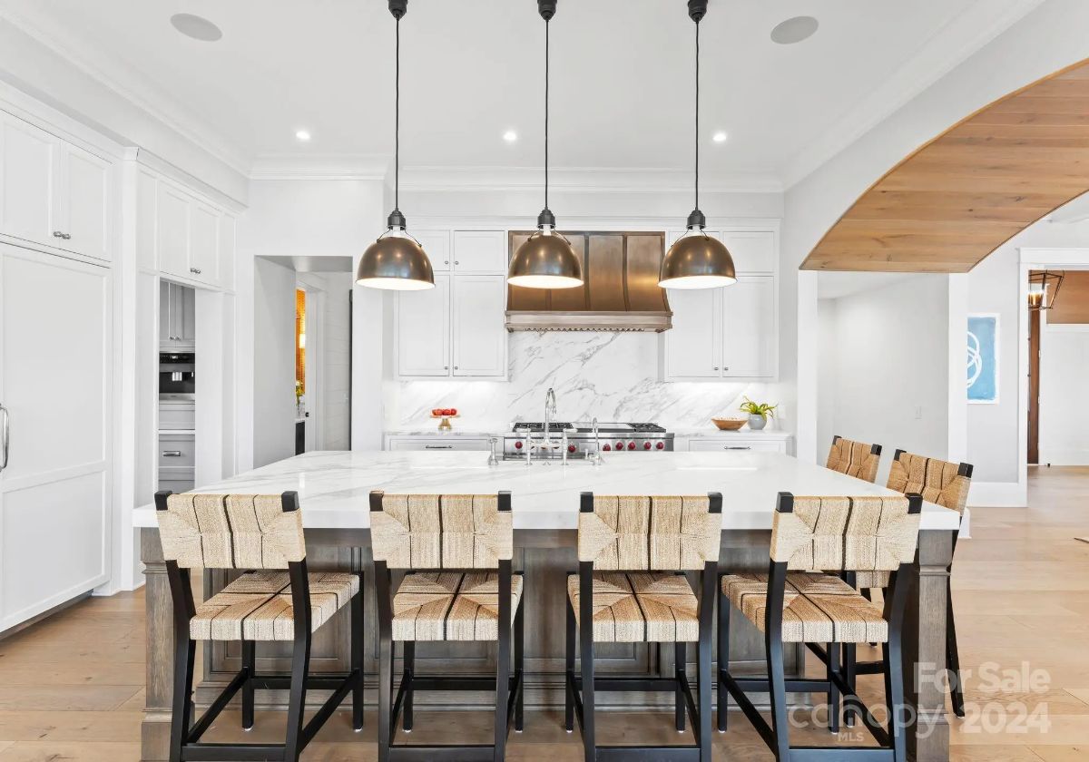 Spacious white kitchen features a large island with seating and stylish pendant lights. 
