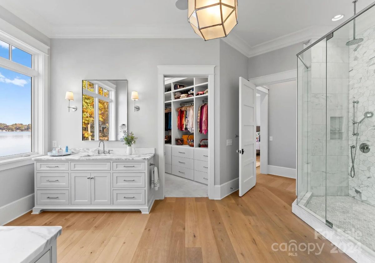 Luxury bathroom includes a walk-in closet, glass shower, and soaking tub with lake views. 