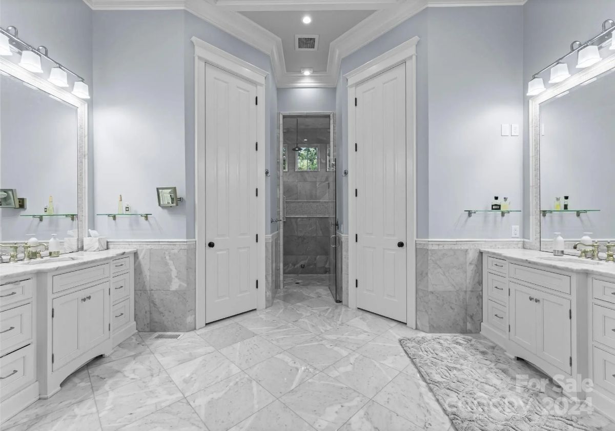 Elegant dual vanity bathroom with marble floors and a central doorway leading to a spacious shower. 