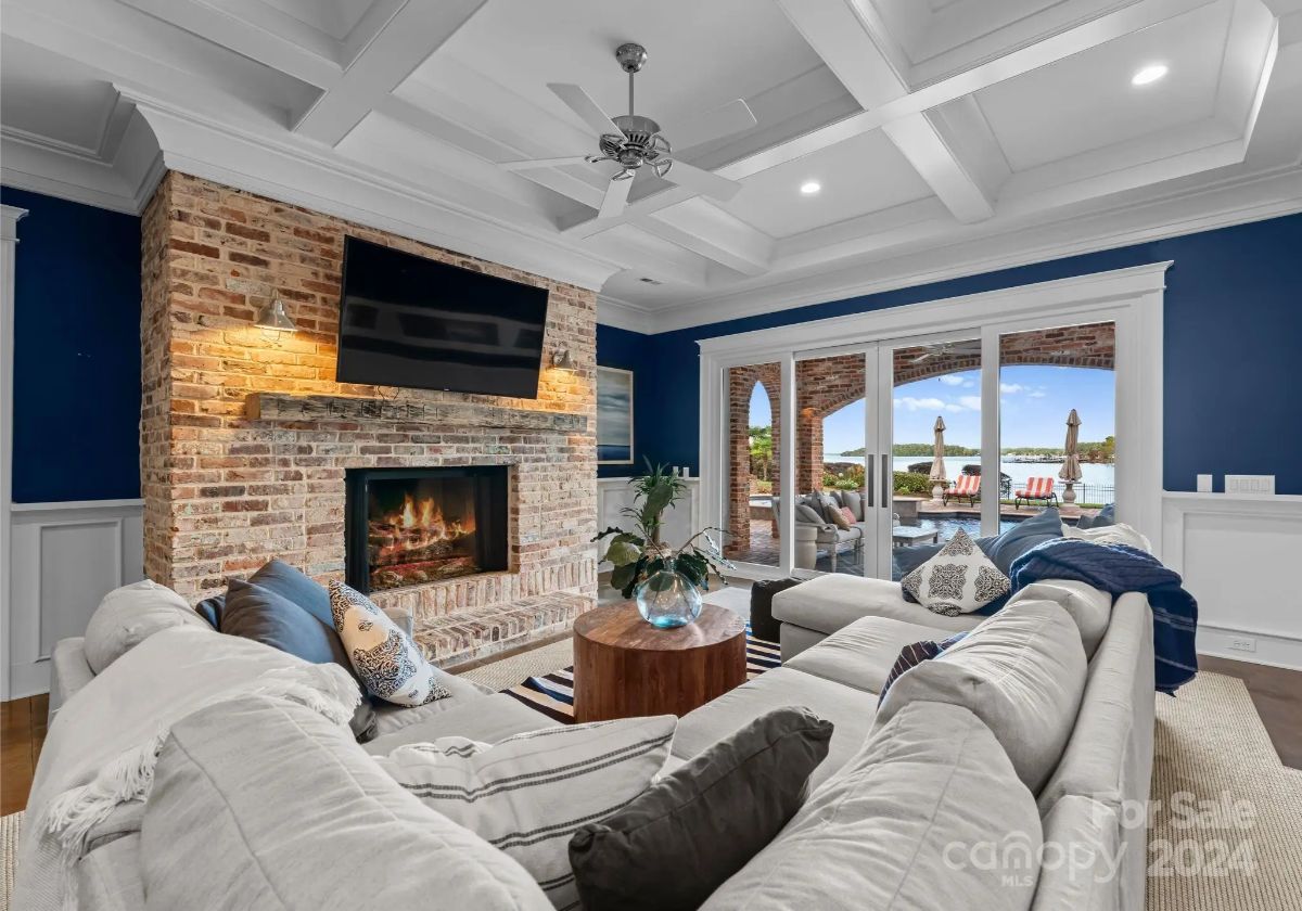 Cozy living room with deep blue walls, coffered ceiling, and a brick fireplace overlooking the patio. 