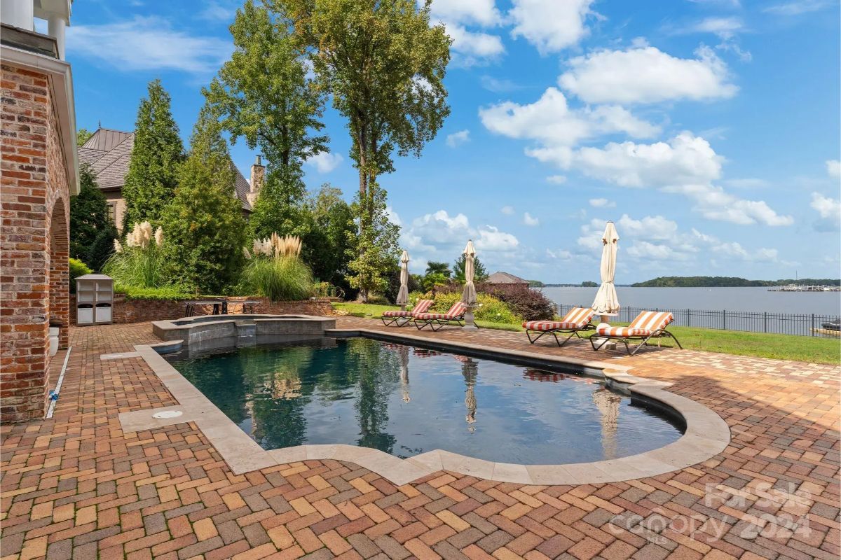 Backyard pool area with brick pavers and scenic water views beyond. 