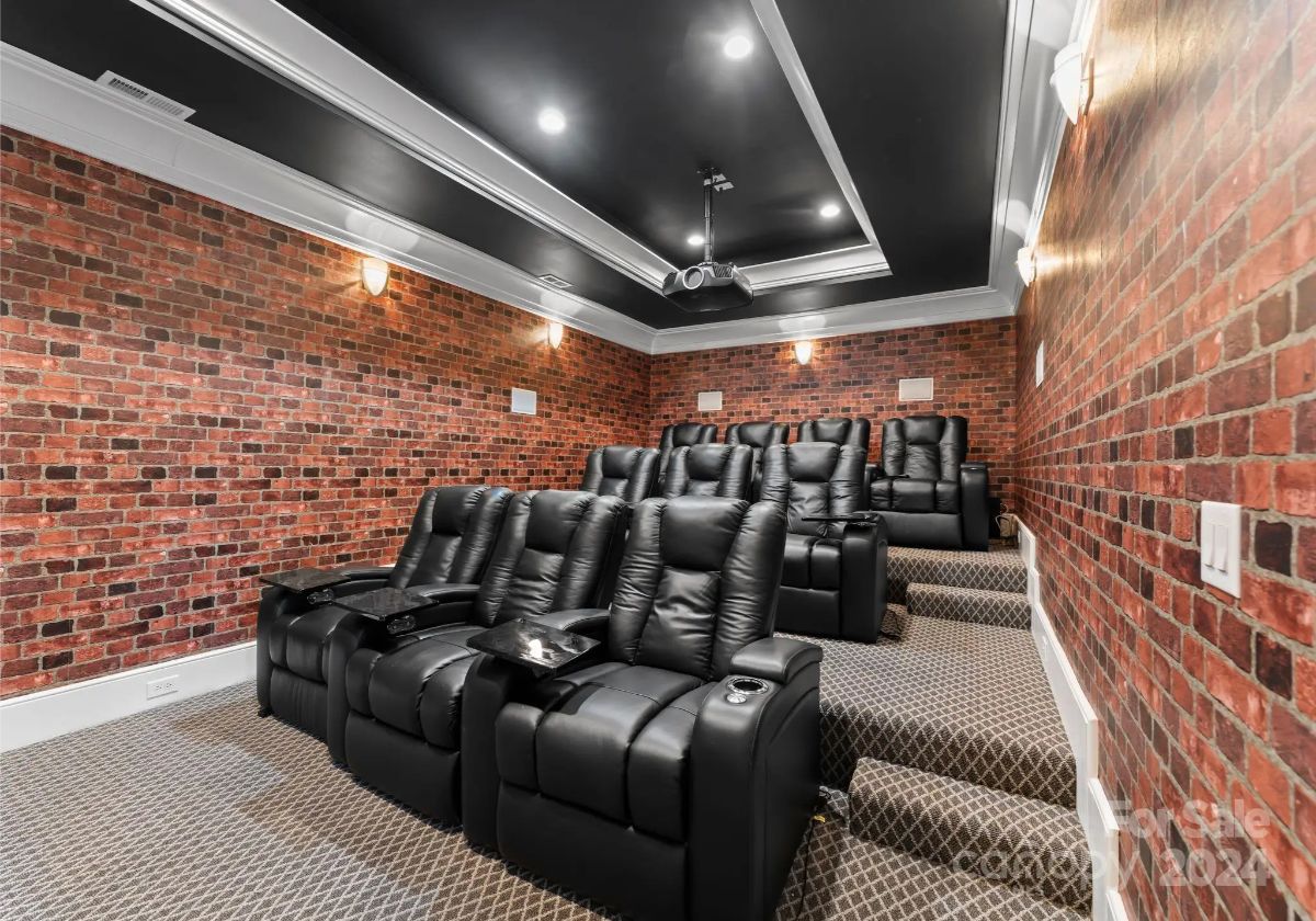 Home theater room with brick walls and tiered leather recliner seating. 