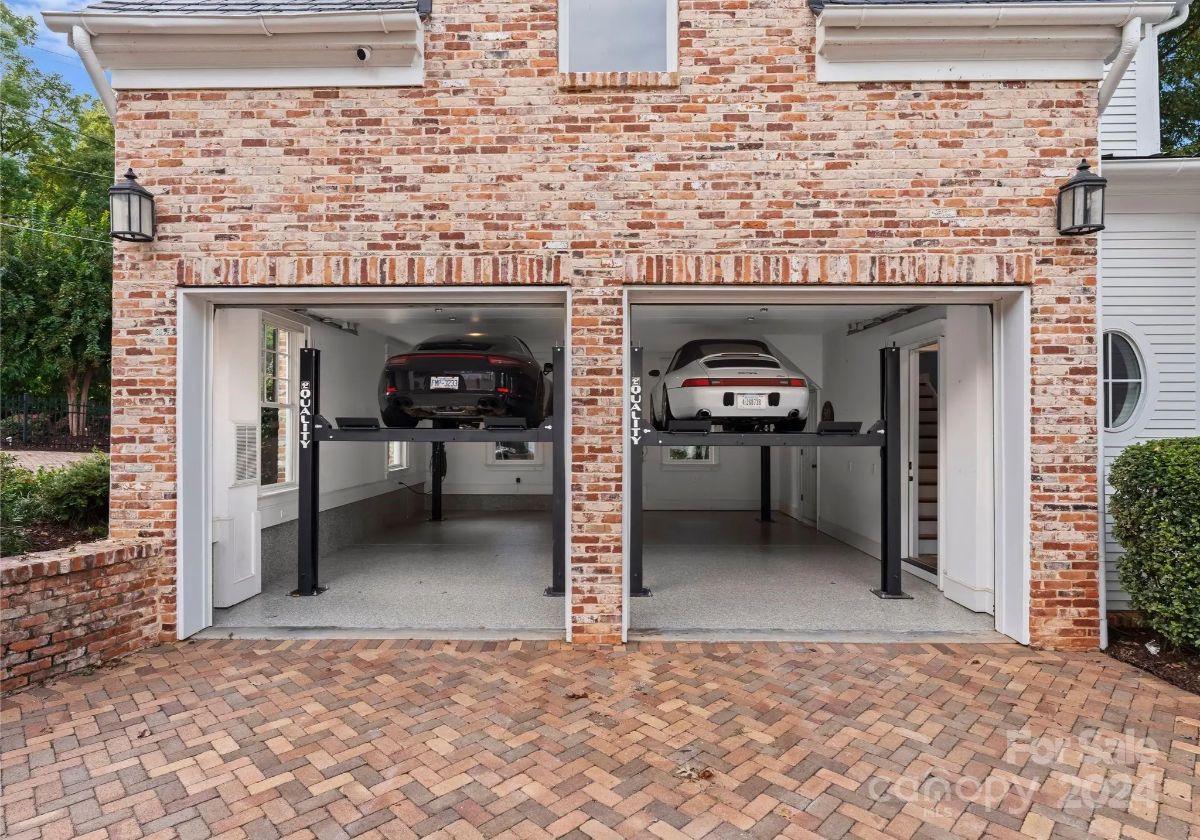 Garage with two cars on lifts in a neatly finished space with matching brick exterior. 