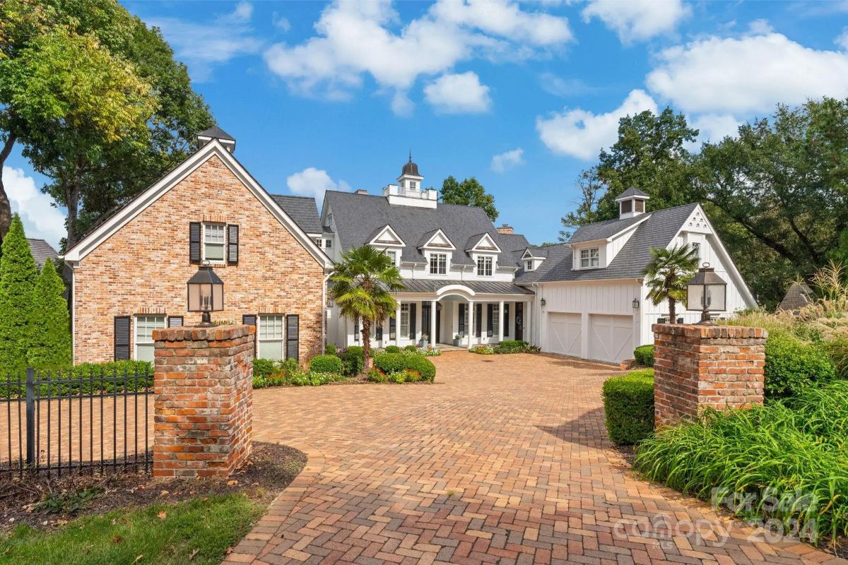 Brick and white-paneled luxury home with a circular driveway and manicured landscaping. 